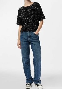 Top corto a maniche corte in paillettes nere abbinato a jeans in denim blu. I jeans hanno una vestibilità rilassata e sono leggermente sbiaditi. Le sneakers completano il look.