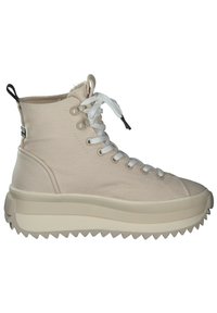 Beige high-top sneakers made of canvas with white laces, thick textured rubber sole, and jagged edge, featuring a small pull tab at the back.