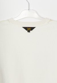 Maglione bianco in cotone con collo a girocollo a coste. Presenta un'etichetta nera e dorata sul retro, che indica marca e taglia.