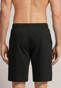 Pantalones cortos negros hechos de tejido ligero, con una cinturilla elástica y dos bolsillos laterales, con un corte recto y bordes dobladillados.