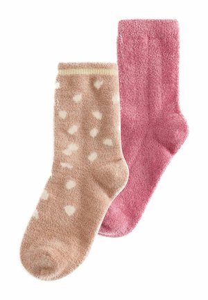 Zwei flauschige Socken, eine einfarbig pink und eine beige mit weißen Herzmustern, nebeneinander auf einem weißen Hintergrund gelegt.