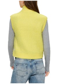 Gelbe Strickweste mit hohem Kragen, von hinten gesehen. Graues Langarmshirt darunter. Getragen mit hellblauen Jeans.