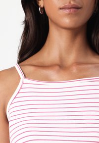 Biały top na ramiączkach z cienkimi różowymi poziomymi paskami. Posiada cienkie, spaghetti ramiączka oraz dopasowany krój, podkreślający gładką, miękką teksturę.