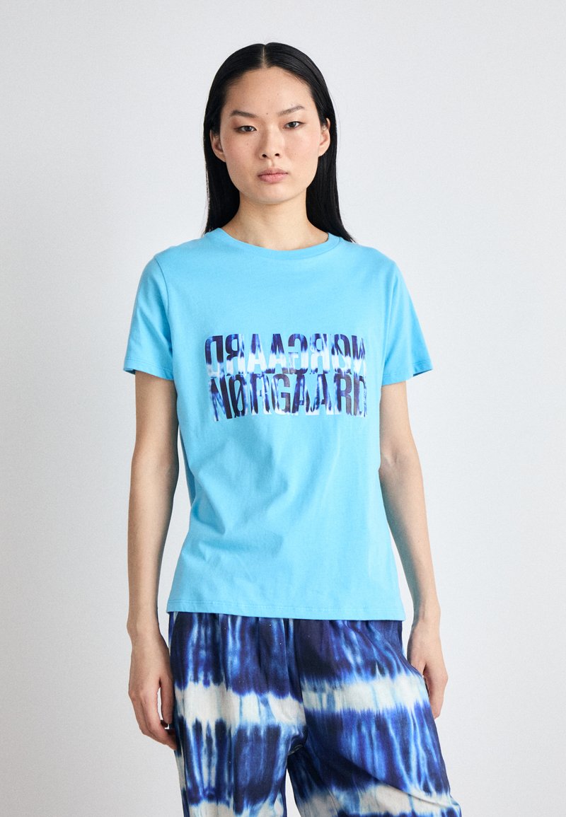 Light blue cotton t-shirt with "morcsaadr" text in multicolored, blurred lettering. Features short sleeves and a round neckline.