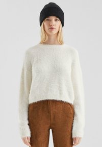Witte, zachte cropped trui met lange mouwen en een geribbelde ronde halslijn, gecombineerd met bruin suede-achtig broek en een zwart gebreide beanie.