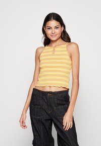 Top cropped amarelo e branco com riscas, com decote em forma de chave e bainha a franzir, combinado com calças escuras de corte largo.