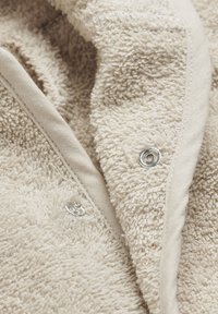 Couverture en tissu éponge beige avec un tissu doux et texturé, un bord beige et des boutons-pression argentés pour une fermeture sécurisée.