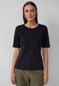 T-shirt noir à manches courtes en coton doux, avec un col rond et une coupe ajustée, présenté avec un pantalon vert olive.