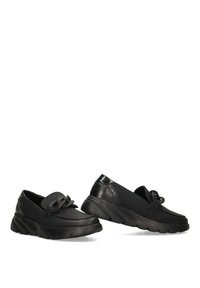 Zapatos negros de tipo slip-on con un empeine liso, un acento texturizado en uno de ellos y un detalle de lazo decorativo. Suela ligera para mayor comodidad y flexibilidad.