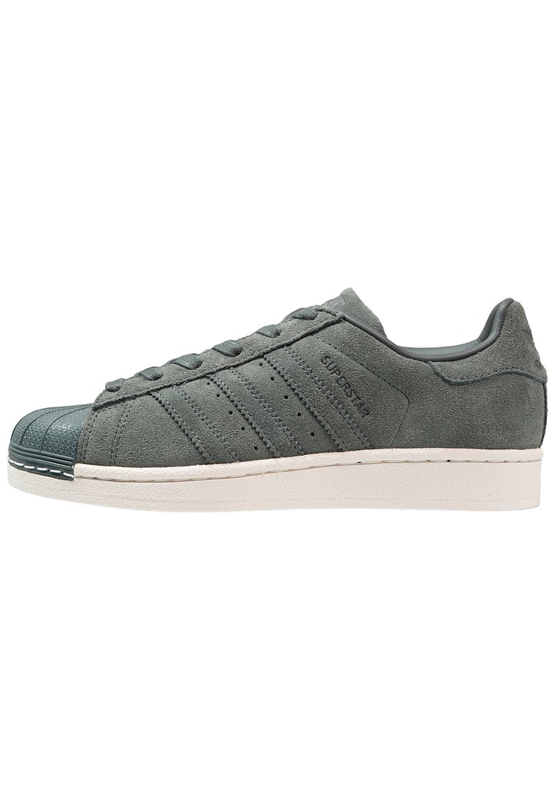 Zapatilla de ante gris oscuro con puntera de goma, cordones texturizados, tres franjas laterales y una suela blanca. Presenta un diseño de corte bajo.