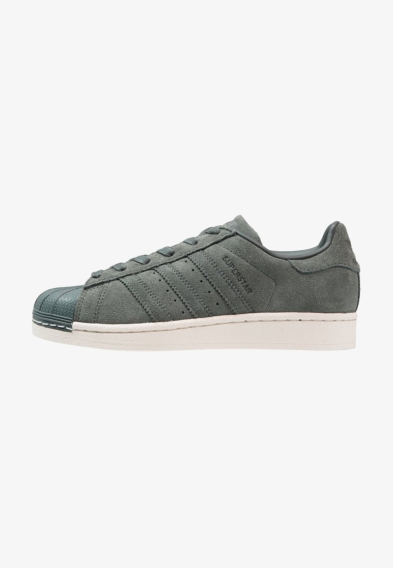 Zapatilla de ante gris oscuro con puntera de goma, cordones texturizados, tres franjas laterales y una suela blanca. Presenta un diseño de corte bajo.