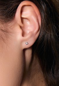Mała srebrna kolczyk wkręcany z pojedynczym przezroczystym kamieniem szlachetnym, zaprezentowany blisko ucha, podkreślający swój okrągły kształt i minimalistyczny design.