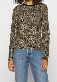 Langärmliges Leopardenmuster-Hemd in Beige und Schwarz, aus weichem Material, mit Rundhalsausschnitt und taillierter Passform. Kombiniert mit blauen Jeans.