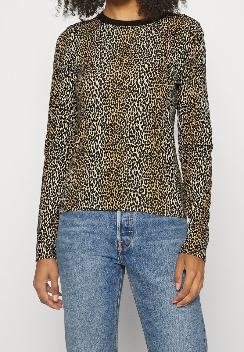 Langärmliges Leopardenmuster-Hemd in Beige und Schwarz, aus weichem Material, mit Rundhalsausschnitt und taillierter Passform. Kombiniert mit blauen Jeans.