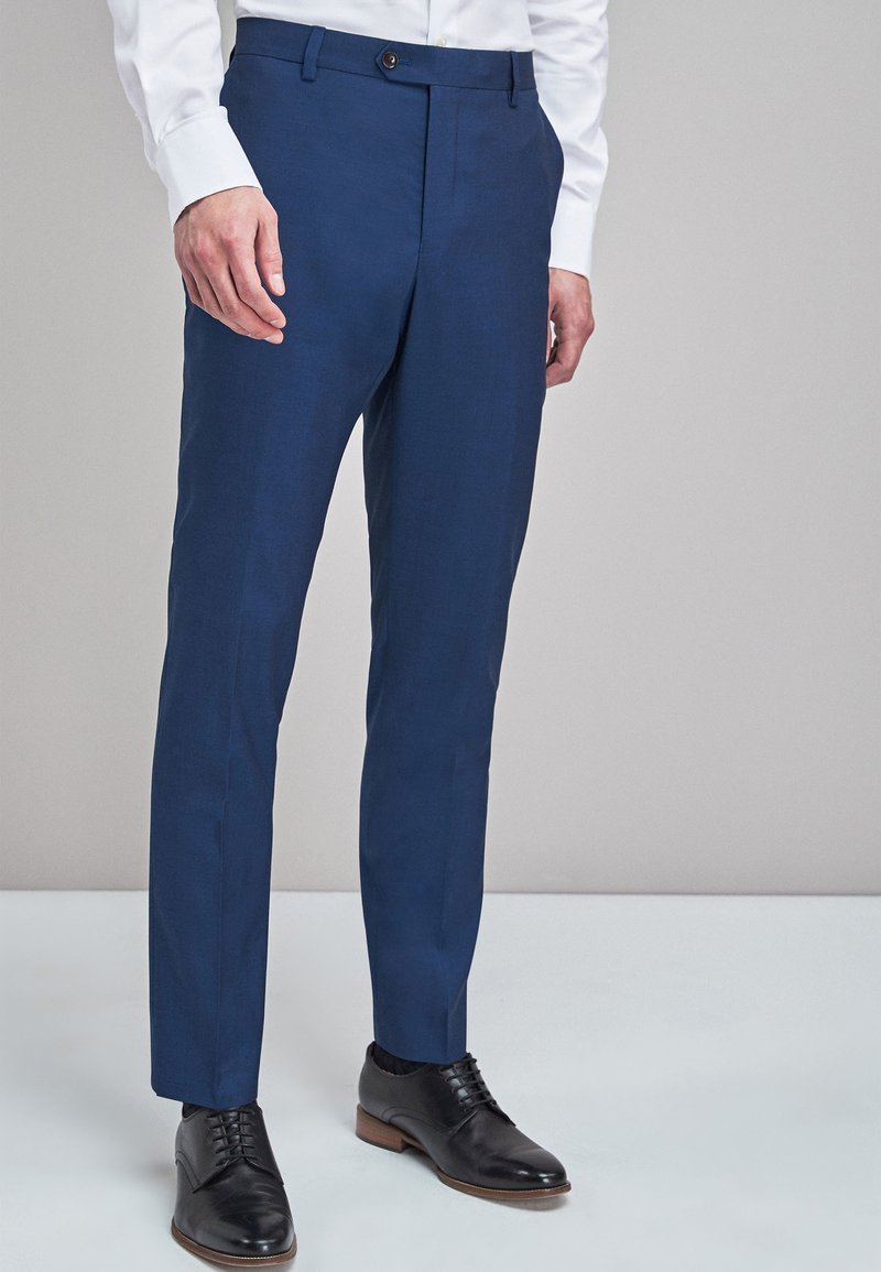 Pantaloni slim-fit blu navy in tessuto texturizzato, dotati di chiusura a un bottone e passanti per cintura, abbinati a scarpe eleganti nere.