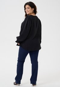 Black long-sleeve top with a round neckline, textured fabric, and puffed sleeves, paired with blue jeans and black heels.
