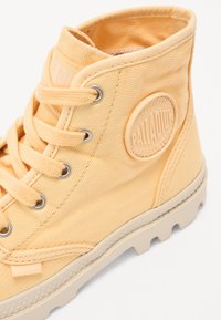 Cizmă ankle din pânză galbenă, cu un logo circular, ochiuri metalice, suprafață texturată și o talpă groasă din cauciuc cu model de aderare.