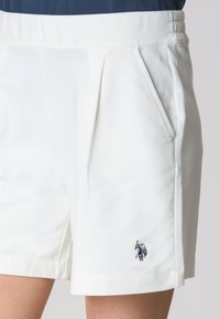Shorts bianchi realizzati in una miscela di cotone, con tasche laterali e un design plissettato. Presenta un piccolo logo ricamato blu sull'orlo.