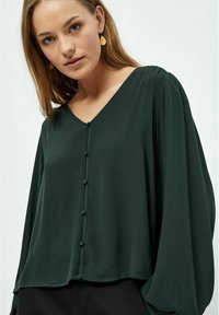 Blusa verde scuro con scollatura a V, dettagli con bottoni sulla parte anteriore e maniche lunghe, leggermente voluminosi, in un tessuto leggero.
