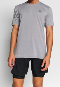 Grå kortärmad sporttröja i lätt material, med rund halsringning och subtil logotyp på vänster bröst.