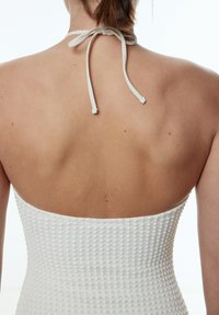 Robe blanche à encolure halter texturée avec un corsage ajusté. Le dos est lisse avec une fermeture à nouer, mettant en valeur la peau et présentant un design simple.
