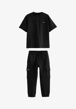 Čierne bavlnené tričko s krátkymi rukávmi a logom na prednej strane, spárované s čiernymi teplákmi s elastickým lemovaním a cargo vreckami.
