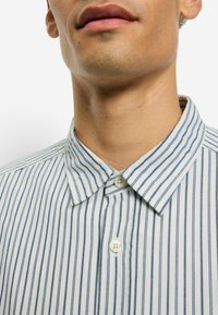 Hemd mit Knopfleiste, marineblauen und weißen vertikalen Streifen, Baumwollstoff, Standardkragen und zwei Knöpfen nahe dem Halsverschluss.