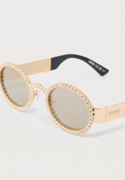 Óculos de sol dourados com lentes redondas, bordados por strass transparentes, apresentando armação transparente e detalhes nas hastes em preto.