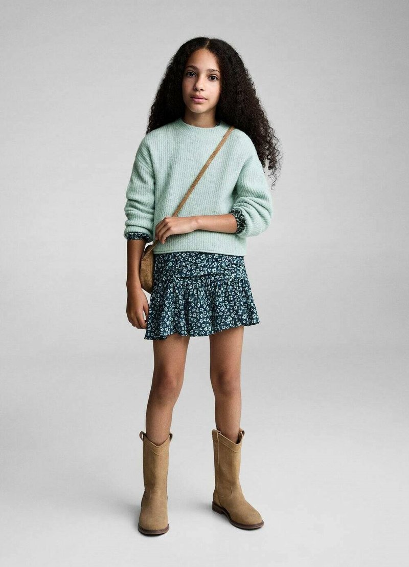 Ljusgrön ribbad tröja, marinblå blommig kjol med volanger och beige knähöga stövlar. Modellen bär en liten axelväska.