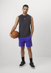 Mustamata käpikute ja Jordan logo'ga must T-särk on kombineeritud siniste korvpallilühikeste pükstega, millel on graafiline disain. Mustad spordijalatsid ja põlvikud.