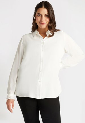Weißes Hemdbluse mit langen Ärmeln, gerafften Manschetten und einem entspannten Schnitt. Glattes Material mit einem leichten Glanz und geschwungenem Saum.