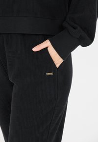 Schwarzes, geripptes Loungewear-Set mit einem Langarmoberteil mit weitem Saum und passenden Hosen mit seitlichen Taschen und einem kleinen Logo-Highlight.