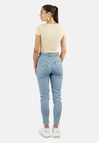 Helltaupe-fitted T-Shirt, kombiniert mit hellblauen, hoch sitzenden Jeans, die Rückentaschen und dezente Markenlogos aufweisen, abgerundet mit weißen Sneakers.