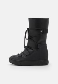 Svart ankelsko med en texturerad överdel, rund tå och snörningsdesign. Har en logotyp-patch och en chunky dold kilklack.