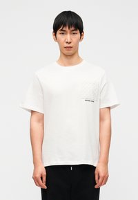 Λευκό βαμβακερό t-shirt με κοντά μανίκια, που διαθέτει τσεπάκι με μοτίβο και σήμα "MICHAEL KORS" κοντά στο τελείωμα.
