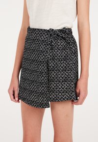 Pantaloni corti neri realizzati in tessuto morbido, con un piccolo motivo geometrico bianco, vita elastica con dettaglio a fiocco e una vestibilità rilassata.