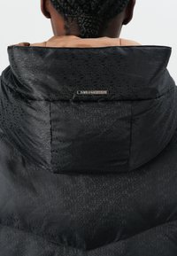 Black puffer jacket featuring a textured pattern with the brand name. The hood is lined in brown, adding contrast to the design.