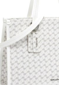 Weiße und graue Handtasche mit Hahnentrittmuster, weißen Griffen und einem silbernen Schlüsselanhänger, der oben befestigt ist.