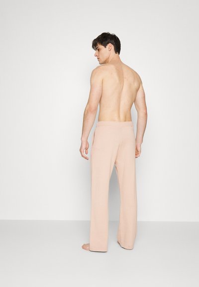 Calças rosa claro com um design de perna reta, faixa elástica na cintura e textura suave, vistas por trás em um modelo com a parte superior do corpo descoberta.