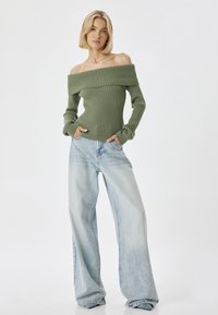 Olivengrüner, schulterfreier Rippstrickpullover; kombiniert mit hellblauen, weit geschnittenen Jeans; weiche Textur; entspannte Passform und lässiger Stil.