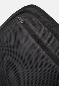 Black mesh bag featuring a textured exterior and a zipper closure, with sturdy stitching and prominent dart shape.