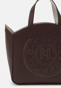 Borsa a spalla in pelle marrone con forma ad arco, caratterizzata da disegni circolari perforati e due manici. Interno foderato con materiale a contrasto.