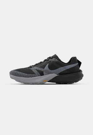 Des chaussures de sport noires et grises avec une tige en maille respirante, une semelle rembourrée et une semelle extérieure en caoutchouc arborant la marque Vibram. Accents réfléchissants visibles.