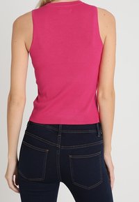 Top sin mangas ajustado de tejido rosa brillante, con textura de canalé y cuello redondo, combinado con jeans azul oscuro con bolsillos traseros.