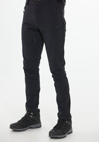 Svarta vattentäta byxor med slim fit, med dragkedjefickor och artikulerade knän. Tillsammans med svarta vandringsskor med grå detaljer.