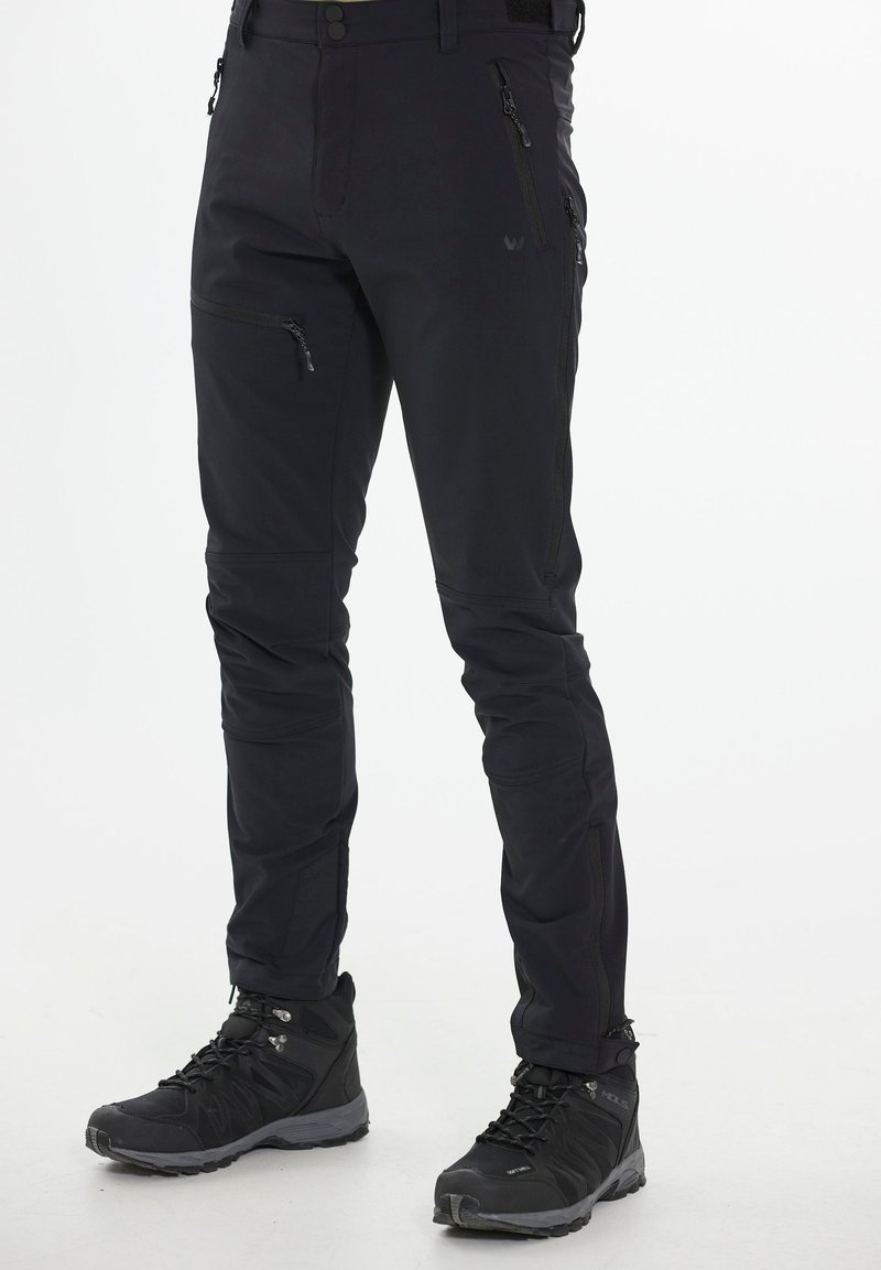 Svarta vattentäta byxor med slim fit, med dragkedjefickor och artikulerade knän. Tillsammans med svarta vandringsskor med grå detaljer.