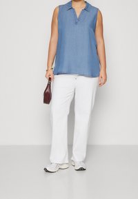 Lysblå ærmeløs denimtop med krave, parret med hvide brede bukser og grå sneakers. Modellen holder en lille burgunder taske.