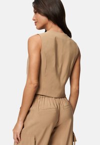 Ärmlös beige topp med en slät textur, rundad halsringning och en avslappnad passform, tillsammans med matchande högmidjade byxor och sidofickor.