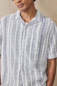 Short-sleeve button-up shirt in white and navy striped linen with a single chest pocket and a camp collar design. Smooth texture.