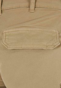Khaki bikses ar gludu tekstūru, ar aizmugures kabatu ar taisnstūra flap, pastiprinātām šuvēm un ciešu piegulšanu ap vidu.